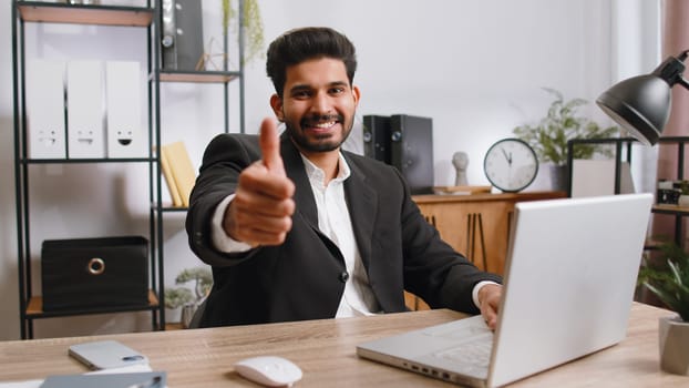 Like. Happy young indian businessman guy working on laptop looking approvingly at camera showing thumbs up, like sign positive something good, positive feedback at office workplace. Freelancer man