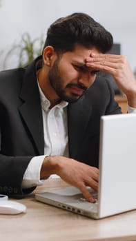 Indian businessman programmer software developer working on laptop loses becoming surprised by bad news results, fortune loss fail at home office. Deadline, bankruptcy. Freelancer man. Vertical shot