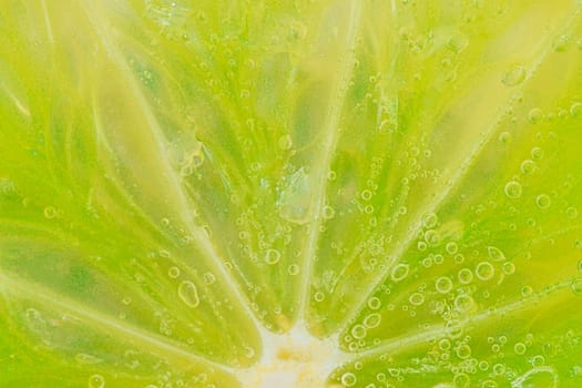 Close-up of a lime slice in liquid with bubbles. Slice of ripe lime in water. Close-up of fresh lime slice covered by bubbles. Macro horizontal image