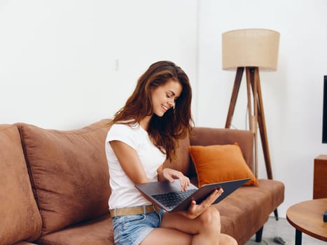 Woman freelancer sitting on the couch with a laptop beautiful smile , modern stylish interior Scandinavian lifestyle, copy space. High quality photo