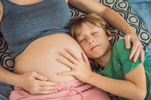 Young beautiful pregnant woman and eldest son. The cute boy leaned his ear against his mother's belly. Expecting a baby in the family concept. Preparing an older child for a younger one.