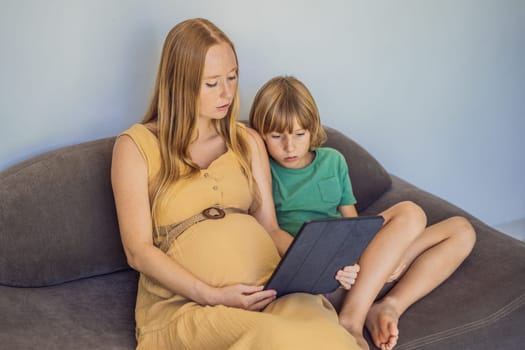 pregnant mom and son look at the tablet. Reading a book or watching a cartoon or making a video call. Look at the photo from the ultrasound.