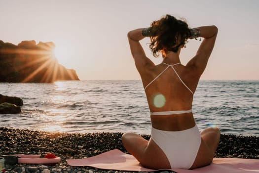 Young woman in swimsuit with long hair practicing stretching outdoors on yoga mat by the sea on a sunny day. Women's yoga fitness pilates routine. Healthy lifestyle, harmony and meditation concept.