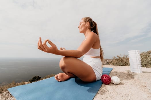 Middle aged well looking woman with black hair doing Pilates with the ring on the yoga mat near the sea on the pebble beach. Female fitness yoga concept. Healthy lifestyle, harmony and meditation.