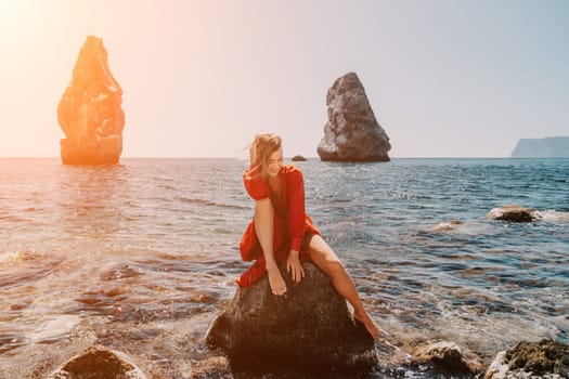 Woman travel sea. Young Happy woman in a long red dress posing on a beach near the sea on background of volcanic rocks, like in Iceland, sharing travel adventure journey