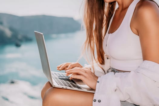 Digital nomad, Business woman working on laptop by the sea. Pretty lady typing on computer by the sea at sunset, makes a business transaction online from a distance. Freelance remote work on vacation