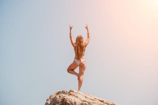 Woman meditating in yoga pose silhouette at the ocean, beach and rock mountains. Motivation and inspirational fit and exercising. Healthy lifestyle outdoors in nature, fitness concept.