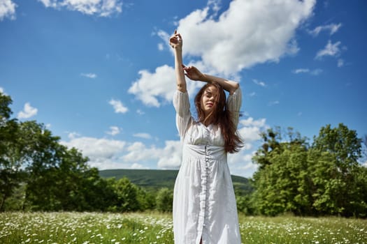 portrait of a happy woman in a light dress in a chamomile field with her hands raised above her head. High quality photo