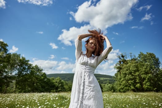 portrait of a happy woman in a light dress in a chamomile field with her hands raised above her head. High quality photo