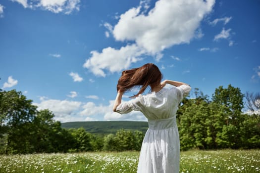 a woman stands in a light dress in a chamomile field and straightens her hair with her hand. High quality photo