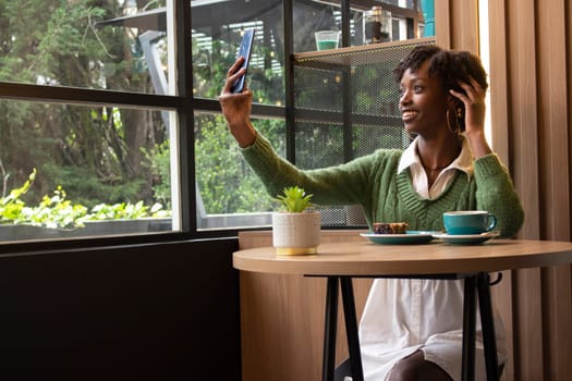 young african american woman sitting in a cafeteria taking a selfie while having a coffee in the city. High quality photo