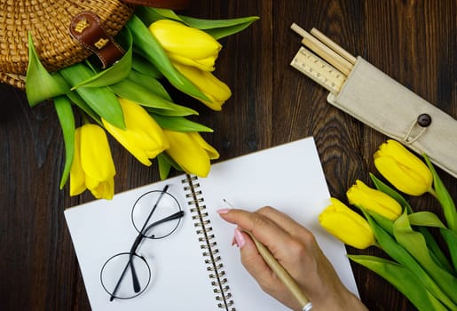 On the table there is a notebook for notes and beautiful yellow tulips. High quality photo