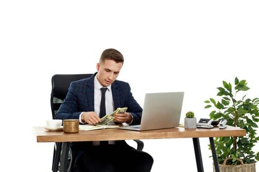 young handsome businessman working on laptop and holding money while sitting on chair at desk.