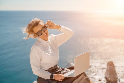 Business woman on nature in white shirt and black skirt. She works with an iPad in the open air with a beautiful view of the sea. The concept of remote work