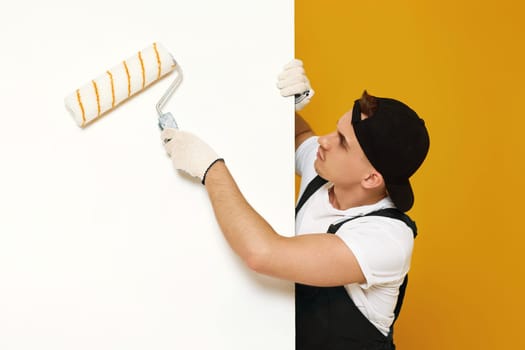 young man in working clothes painting white walls in the room. copy space for text