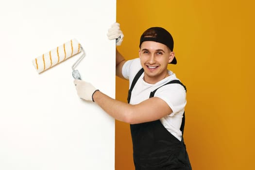 happy man in working clothes painting white walls in the room. copy space for text