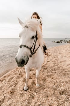 A white horse and a woman in a dress stand on a beach, with the sky and sea creating a picturesque backdrop for the scene