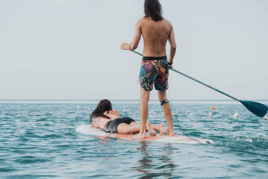 Sea woman and man on sup. Silhouette of happy young woman and man, surfing on SUP board, confident paddling through water surface. Idyllic sunset. Active lifestyle at sea or river