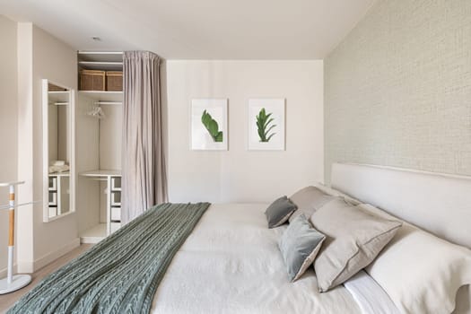 Comfortable bright bedroom with double bed and an empty wardrobe for clothes with beige wallpaper and cute pictures on the wall. The concept of moving to a new apartment.