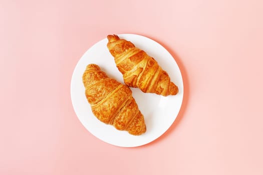 Plate with delicious croissants on a pink background. french pastries. copy space.