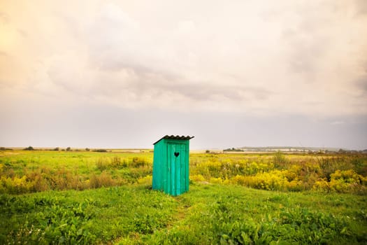 wooden toilet with a carved window in the shape of a heart, an open field.