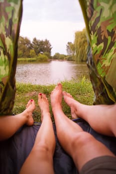 A small camping tent on the lake, a night's lodging and the feet of a young couple.