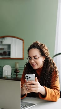 Smiling Young woman using smartphone for remote work and e-learning at home. Modern Technology: Young Woman Using Smartphone for Work and Learning at Home. Pretty woman holding mobile phone.