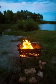 evening landscape - burning firewood in the grill: preparation for the frying of meat, near the lake.