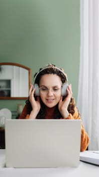 Young happy woman student wearing headphone using laptop elearning at home office listening music, live lecture or podcast webinar, learning language on online seminar sitting at desk with computer