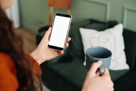 Mockup Smartphone Display: Woman Holding Coffee and Texting on Cellphone Apps, Over Shoulder View for Advertising and Promotions. smartphone with a blank screen for mobile application layout.