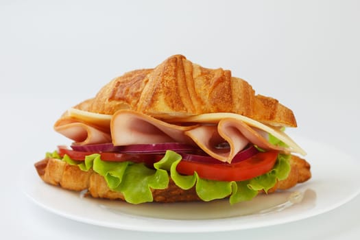 Croissant sandwich with ham, cheese, tomato and lettuce on white background