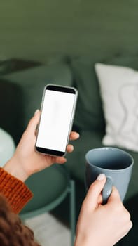 Modern Woman Using Smartphone and Coffee with White Mockup Screen for Advertising. Mockup Smartphone in Female Hands with Coffee, Over Shoulder View of Mobile Apps in Use, Advertising Concept.