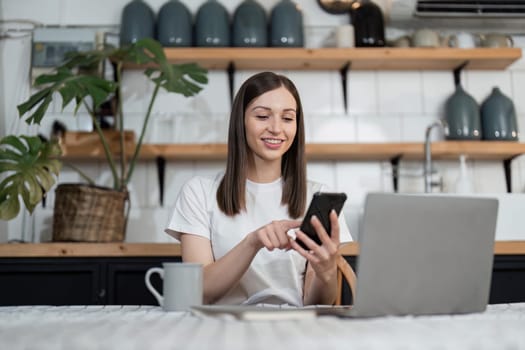 Happy woman using mobile phone during breakfast time in the kitchen. Young happy woman enjoying in morning time at the kitchen while text messaging on smart phone.