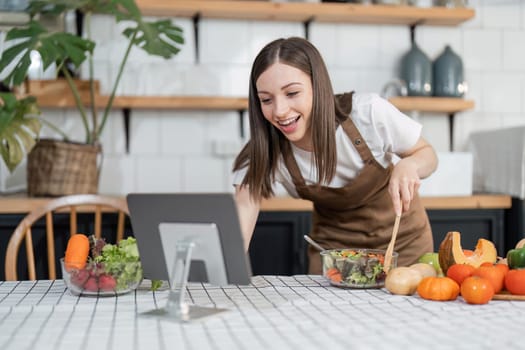 Image of young pretty lady in kitchen and cooking the salad. Looking at tablet computer.