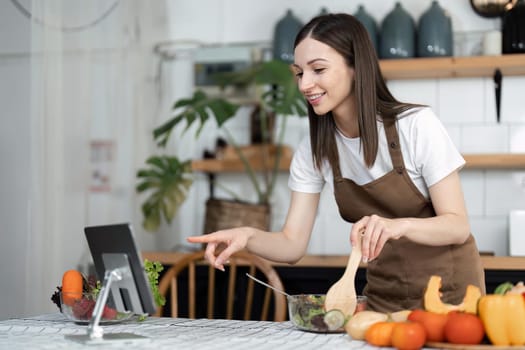 Image of young pretty lady in kitchen and cooking the salad. Looking at tablet computer.