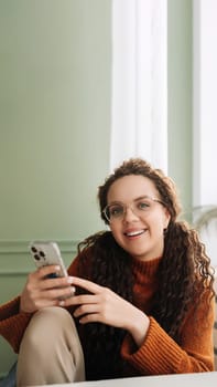 Happy woman using cell phone technology at home, smiling while checking apps on her smartphone and relaxing with cellular devices in hand