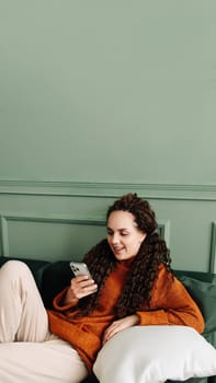 Happy relaxed young woman sitting on couch using cell phone, smiling lady laughing holding smartphone, looking at cellphone enjoying doing online ecommerce shopping in mobile apps or watching videos.