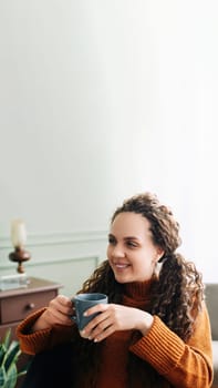 Cozy Winter Mornings: Happy Woman Enjoying Warm Drink and Daydreaming at Home. Warmth and Relaxation: Young Woman Holding a Cup of Coffee and Daydreaming at Home