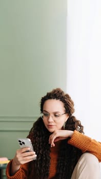 Stylish woman browsing on smartphone at home for online shopping. Young woman wearing glasses checking apps on cellphone at home. Happy woman using smartphone for online shopping and browsing.
