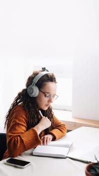 Young woman elearning from home, attending virtual class and remote conference meetings on laptop. Female student distance learning at home with laptop, headphones, and webinars.