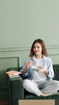 Contented Student Taking a Break from Online Classes: Food, Books, and Laptop on Sofa. Happy Female Student Taking a Break from Online Studies with Delicious Meal and Books.