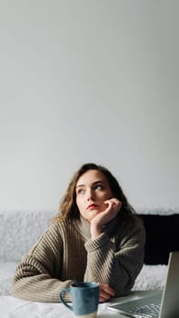 Creative woman working from home writing lesson plan and schedule for students, using laptop and sipping coffee at kitchen table. Productive teacher writes outline and schedule at laptop.