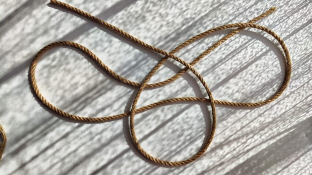 Jute twisted rope lying on a white surface with shadows from the sun. Abstract background, texture, pattern, frame