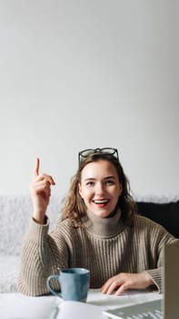 Eureka Excited female entrepreneur with successful business idea, sitting at kitchen table with laptop and showing index finger, ready to make a brilliant project and business plan.
