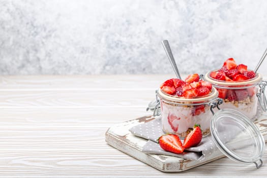 Parfait with Fresh Strawberries, Yoghurt and Crunchy Granola in Transparent Glass Mason Jars on White Rustic Wooden Background Angle View, Healthy Breakfast or Light Summer Dessert, Copy Space