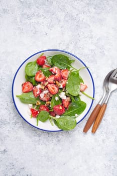 Light Healthy Summer Salad with fresh Strawberries, Spinach, Cream Cheese and Walnuts on White Ceramic Plate, white rustic stone Background Top View.