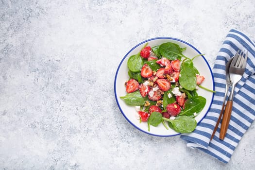 Light Healthy Summer Salad with fresh Strawberries, Spinach, Cream Cheese and Walnuts on White Ceramic Plate, white rustic stone Background From Above, Space For Text.