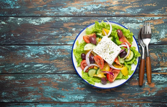 Traditional Greek Salad with Feta Cheese, Tomatoes, Bell Pepper, Cucumbers, Olives, Herbs in white ceramic bowl on blue rustic wooden table background from above, Cuisine of Greece. Space for text