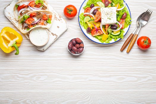 Traditional Greek Food: Greek Salad, Gyros with meat and vegetables, Tzatziki sauce, Olives on White rustic wooden table background from above. Cuisine of Greece. Copy space