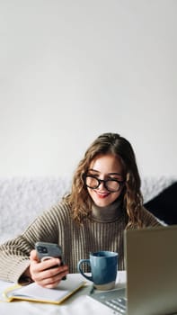 SMM specialist working from home at kitchen table, using smartphone to select blogger for product promotion in social media, in front of laptop. Influencer marketing concept.